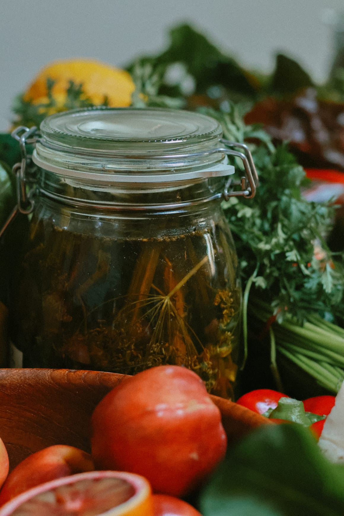 Jar of fermenting fennel honey surrounded by fruits and vegetables